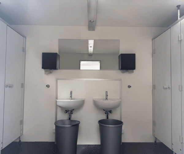Damenbereich eines mobilen Toilettenwagens mit zwei Waschbecken, Spiegel, Papierhandtuchspendern und mehreren abschließbaren WC-Kabinen – PZV Elting Emsdetten.