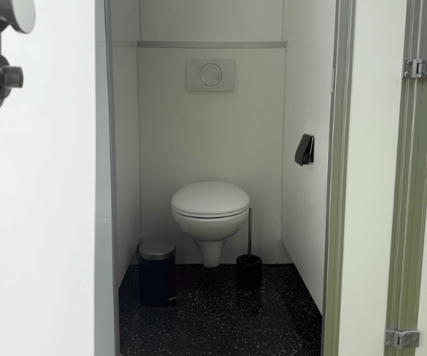 Innenansicht einer einzelnen WC-Kabine im Toilettenwagen XXL von PZV Elting mit wandhängender Toilette, Papierhalter, Hygienebürste und Abfalleimer.