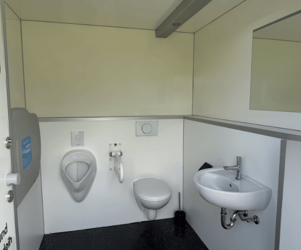 Innenansicht eines barrierefreien Toilettenwagens mit WC, Urinal, Waschbecken, Spiegel und Haltegriff – PZV Elting Emsdetten.